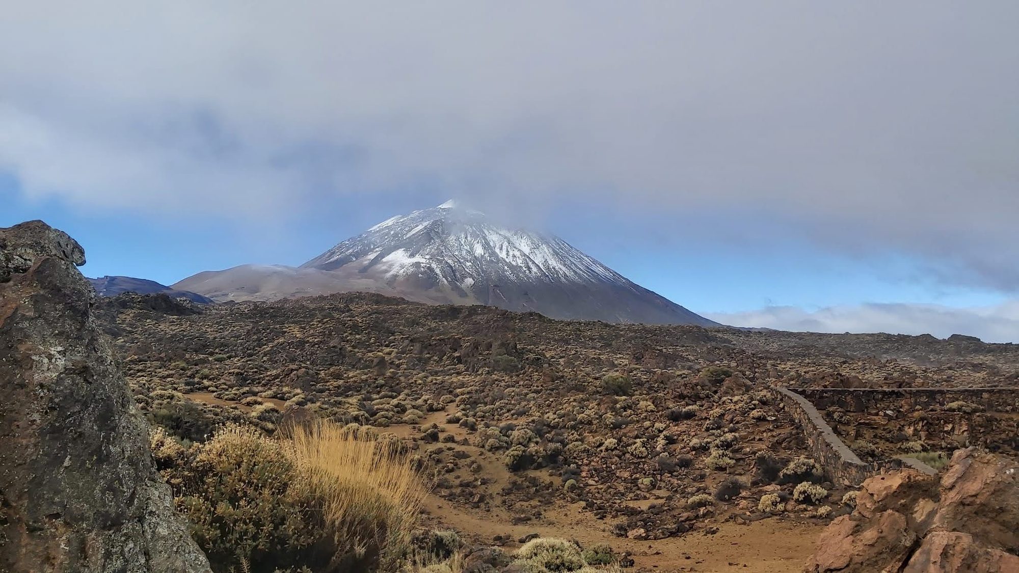 Pico del Teide nevado entre nubes sobre el paisaje volcánico rocoso de Tenerife.